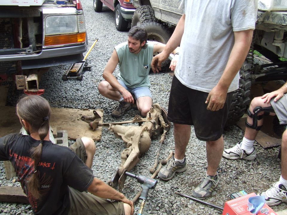 Front of a lifted 1992 Ford Bronco with its hood open, being worked on by several people