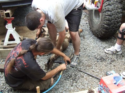 1995 Ford Bronco - Two mechanics work on a vehicle's axle assembly, with a large off-road tire visible in the background.