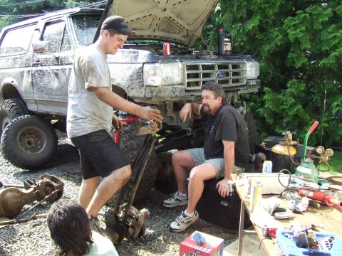 1995 Ford Bronco - Two men are working on a lifted Ford Bronco in a yard, with tools and parts laid out.