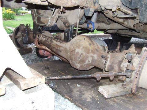 1995 Ford Bronco - A person works on the rear axle assembly of a vehicle, which is raised for maintenance.