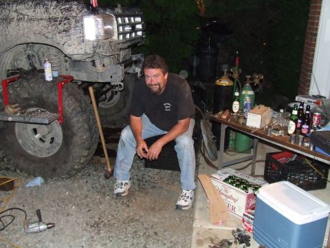 1995 Ford Bronco - A man relaxes next to a custom off-road vehicle, with a table of drinks and tools in the background.