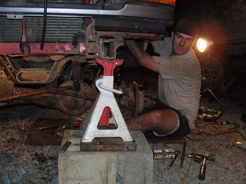 1995 Ford Bronco - A mechanic works on the front end of a vehicle that is elevated on jack stands.