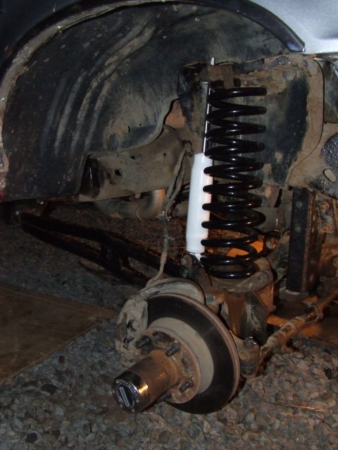 1995 Ford Bronco - Close-up of a lifted front suspension system, a coil spring and shock absorber, with visible text on the hub.