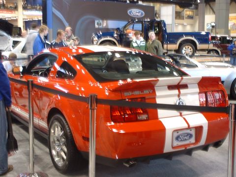 2000 Ford Crown Victoria - Rear view of an orange 2007 Ford Mustang Shelby GT500 with white racing stripes and Shelby badging on display.
