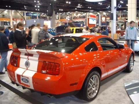 2000 Ford Crown Victoria - Rear view of an orange Ford Mustang GT with white racing stripes at an auto show.