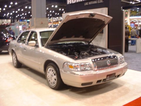 2000 Ford Crown Victoria - Silver Mercury Grand Marquis on display at an auto show, with its hood open to reveal the engine.