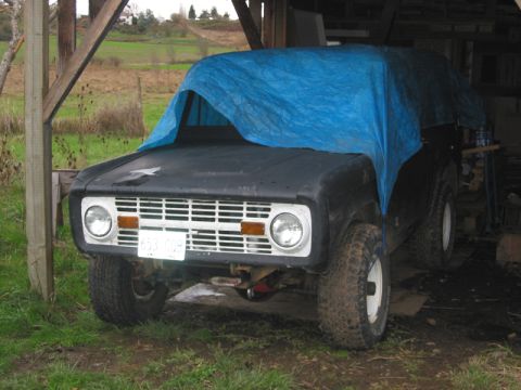 1968 Ford Bronco - A 1968 Ford Bronco is partially covered by a blue tarp while parked in a rustic shelter.