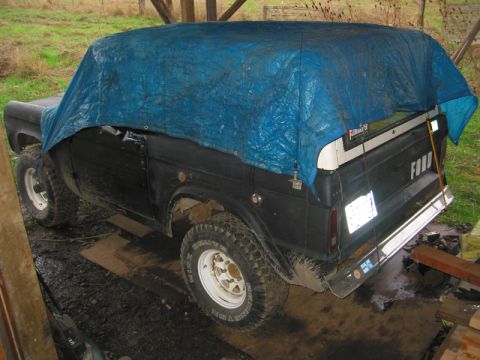 1968 Ford Bronco - A 1968 Ford Bronco is partially covered by a blue tarp, parked outdoors under a shelter.