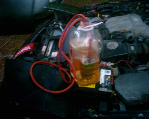 1994 Ford Probe - The engine bay of a 1994 Ford Probe shows a makeshift fluid transfer setup with a large bottle and hoses connected to the engine.