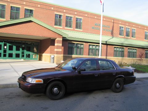 1991 Ford LTD Crown Victoria - A dark sedan is parked on the asphalt in front of Merrimack Middle School, with the school's name visible on the brick building.