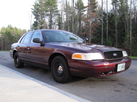 1991 Ford LTD Crown Victoria - This maroon Ford Crown Victoria is parked curbside with a wooded area behind it.