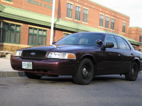 1991 Ford LTD Crown Victoria - This dark sedan, likely a Ford Crown Victoria Police Interceptor, is parked on a street in front of a brick building.