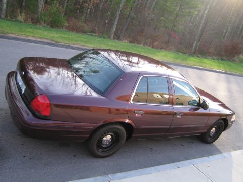 1991 Ford LTD Crown Victoria - A maroon sedan is parked on the side of a road, with trees in the background.