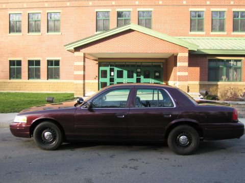 1991 Ford LTD Crown Victoria - Side view of a maroon police sedan parked in front of a brick building with green doors.