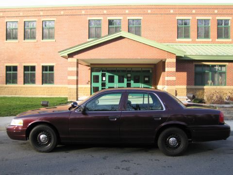 1991 Ford LTD Crown Victoria - A maroon Ford Crown Victoria sedan, likely a police interceptor model, is parked outside a brick building.
