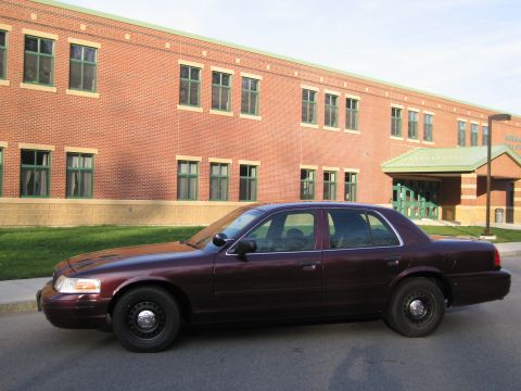 1991 Ford LTD Crown Victoria - A maroon Ford Crown Victoria sedan is parked on the street in front of a brick building with green trim.