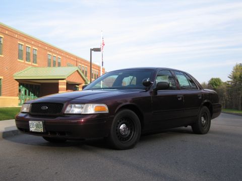 1991 Ford LTD Crown Victoria - This sedan, likely from the early 2000s, is parked on a paved road in front of a school building.
