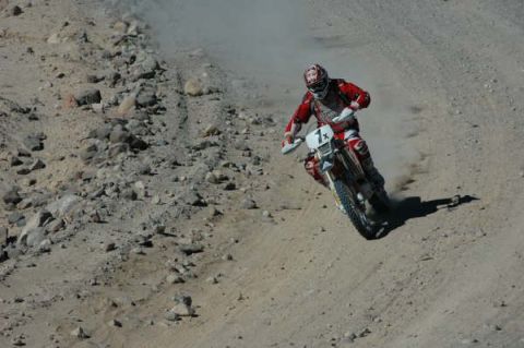 1990 Ford Bronco - motorcycle racer in red gear and number plate 1x rides at speed through a rocky, dusty desert wash.