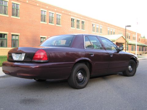 1991 Ford LTD Crown Victoria - This maroon sedan is seen from the rear three-quarter angle, parked on a street in front of a brick building.