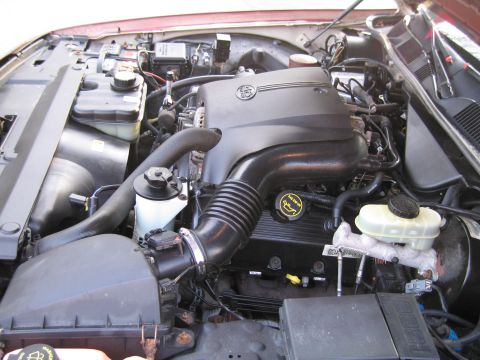 1991 Ford LTD Crown Victoria - The engine bay of a vehicle, a V8 badge on the engine cover and various hoses and components.