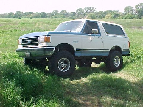 1990 Ford Bronco - This lifted Ford Bronco is shown from a three-quarter front angle in a grassy field.