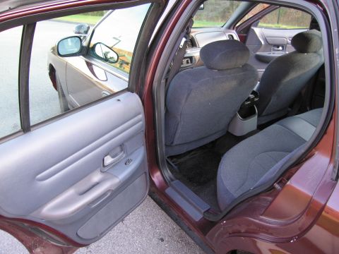1991 Ford LTD Crown Victoria - The interior of a maroon Ford Crown Victoria shows the rear seats and door panel with the exterior visible through the open door.