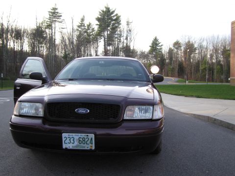1991 Ford LTD Crown Victoria - A dark red Ford Crown Victoria is parked on a road with trees in the background and its driver's door ajar.