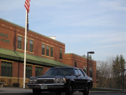1991 Ford LTD Crown Victoria - A black 1991 Ford Crown Victoria LTD is parked in front of a brick school building under a blue sky.