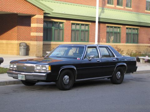 1991 Ford LTD Crown Victoria - A black Ford Crown Victoria is parked in front of a brick building with green trim.
