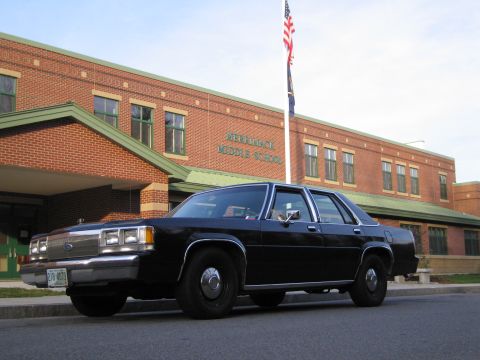 1991 Ford LTD Crown Victoria - A black 1991 Ford Crown Victoria LTD is parked in front of Merrimack Middle School, with an American flag flying above.