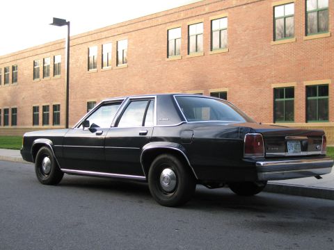 1991 Ford LTD Crown Victoria - Rear view of a black 1991 Ford Crown Victoria LTD parked on a street in front of a brick building.