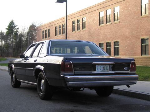 1991 Ford LTD Crown Victoria - Rear view of a black 1991 Ford Crown Victoria LTD sedan parked on a street in front of a brick building.
