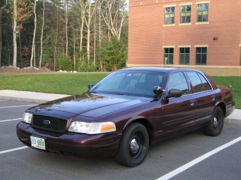 1991 Ford LTD Crown Victoria - A dark red Ford Crown Victoria Police Interceptor is parked in a lot with a brick building in the background.
