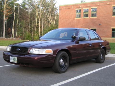 1991 Ford LTD Crown Victoria - A maroon Ford Crown Victoria sedan is parked in a lot with a brick building in the background.