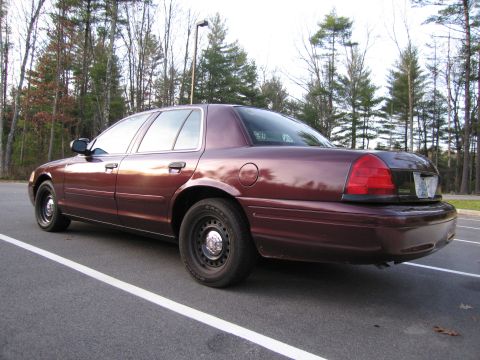 1991 Ford LTD Crown Victoria - The rear quarter panel of a maroon sedan is visible, parked in a lot with trees behind it.