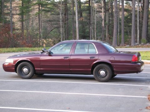 1991 Ford LTD Crown Victoria - This maroon sedan, likely a 2000s Ford Crown Victoria, is seen from the side in a parking lot with trees in the background.