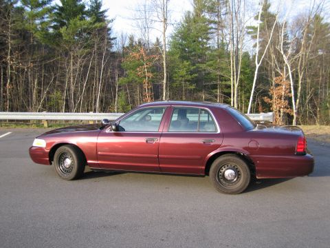 1991 Ford LTD Crown Victoria - Side view of a maroon sedan parked on asphalt with a wooded area behind it.