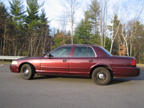 1991 Ford LTD Crown Victoria - This maroon Ford Crown Victoria is seen from the side, parked near a wooded area.