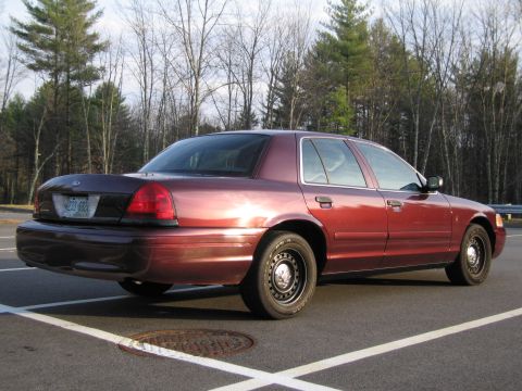 1991 Ford LTD Crown Victoria - This red sedan is seen from the rear quarter angle in a parking lot with trees in the background.