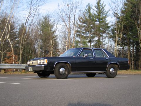 1991 Ford LTD Crown Victoria - This black sedan, identified as a 1988 Ford Crown Victoria, is parked on the roadside with trees in the background.