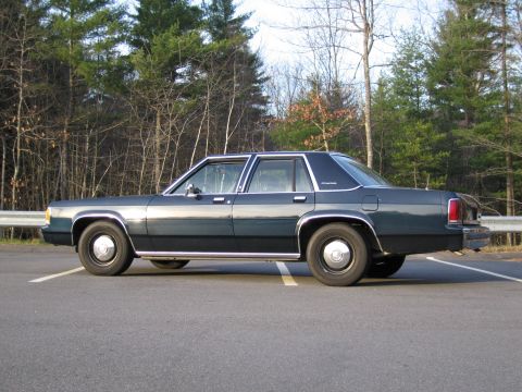 1991 Ford LTD Crown Victoria - A dark green 1991 Ford Crown Victoria LTD sedan is parked on asphalt with trees in the background.