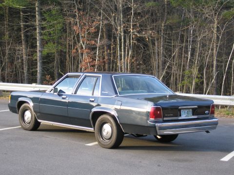 1991 Ford LTD Crown Victoria - This dark blue sedan, likely a 1990 model, is seen from the rear in a parking lot.