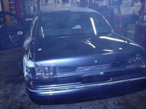 1996 Ford Crown Victoria - Rear view of a dark blue sedan undergoing repairs in a workshop, with the driver's door ajar.
