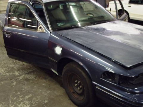 1996 Ford Crown Victoria - A dark blue sedan is undergoing refinishing, with its hood up and doors open, revealing primer on the fender.