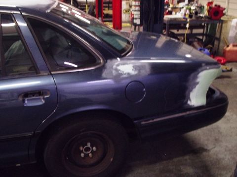1996 Ford Crown Victoria - The rear quarter panel of a blue Ford Crown Victoria is prepped for paint, with visible primer and body filler.