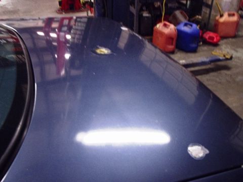 1996 Ford Crown Victoria - Close-up of a blue car's hood, showing reflections and minor surface damage.