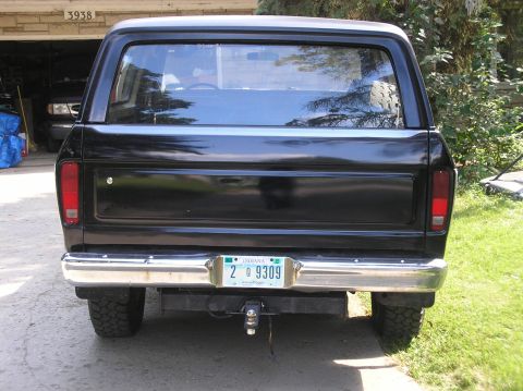 1978 Ford Bronco - This black Ford Bronco is parked in front of a garage, showing its rear end and license plate.