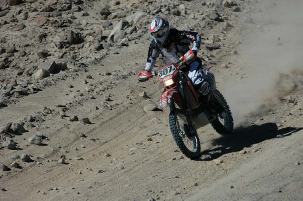 Off-road dirt bike racer number 307 riding a red motorcycle on a rocky desert trail