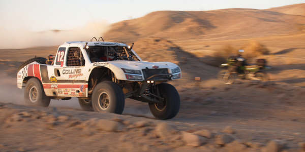 White Collins Motorsports off-road race truck number 12 speeding through desert at dusk