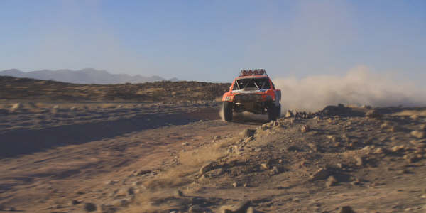 Red off-road race truck driving across open desert with distant mountains